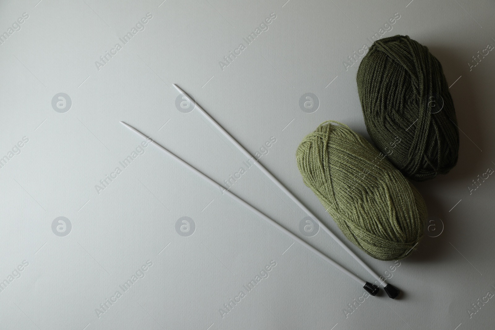 Photo of Soft green yarns and metal knitting needles on light background, flat lay. Space for text