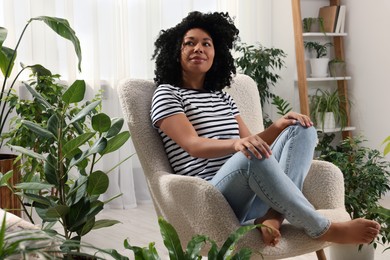 Woman relaxing in armchair surrounded by beautiful houseplants at home