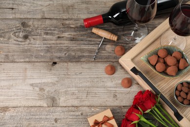 Photo of Red wine, chocolate truffles, corkscrew, roses and gift box on wooden table, flat lay. Space for text