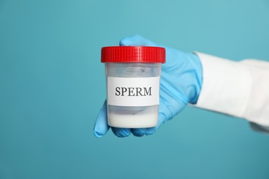 Scientist holding container with sperm on turquoise background, closeup