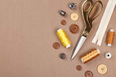 Photo of Different sewing supplies on brown fabric, flat lay. Space for text