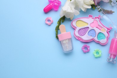 Photo of Decorative cosmetics for kids. Eye shadow palette, lipsticks, accessories and flowers on light blue background, flat lay. Space for text