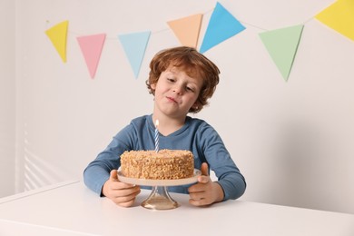 Photo of Cute boy with birthday cake at white table indoors