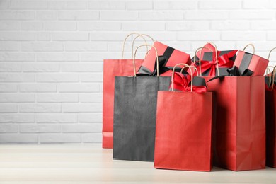 Photo of Paper shopping bags and gift boxes on table near white brick wall, space for text. Black Friday sale