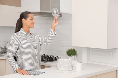 Photo of Young woman holding clean glass in kitchen. Dish washing