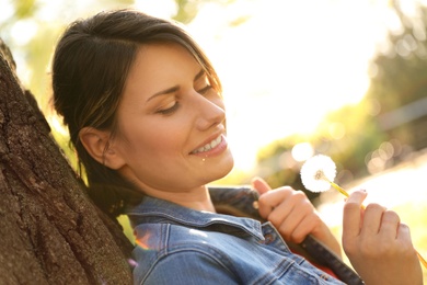 Photo of Young woman with dandelion in park on sunny day. Allergy free concept