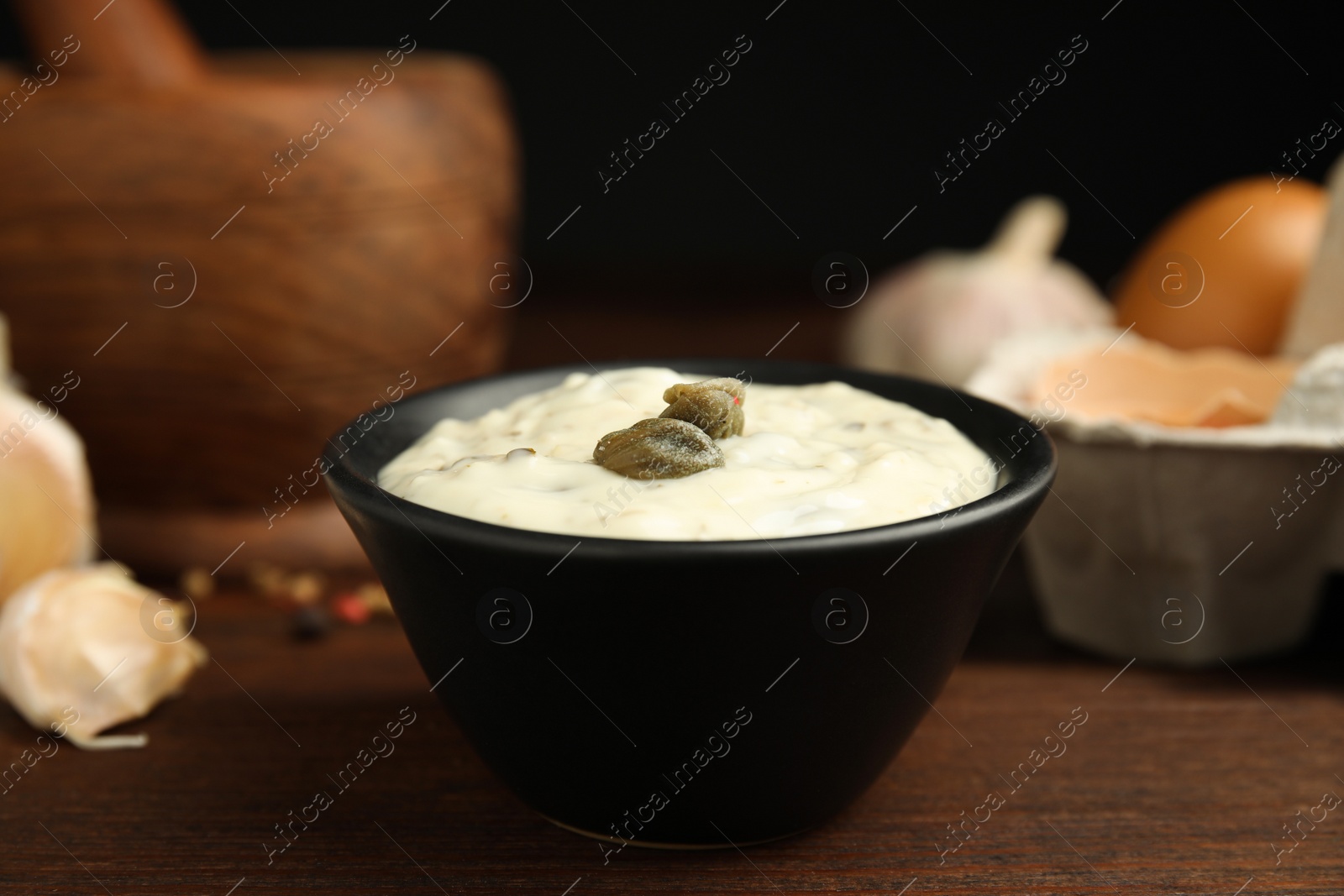 Photo of Creamy caper sauce in bowl on wooden table, closeup