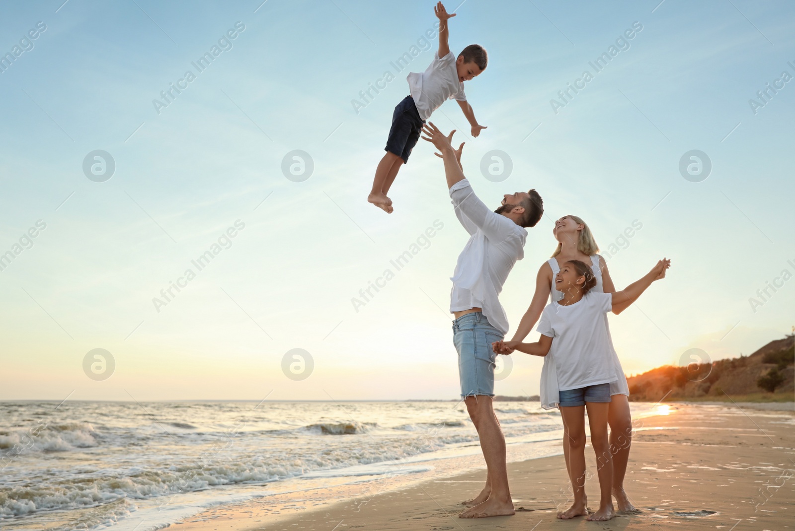 Photo of Happy family having fun on sandy beach near sea at sunset