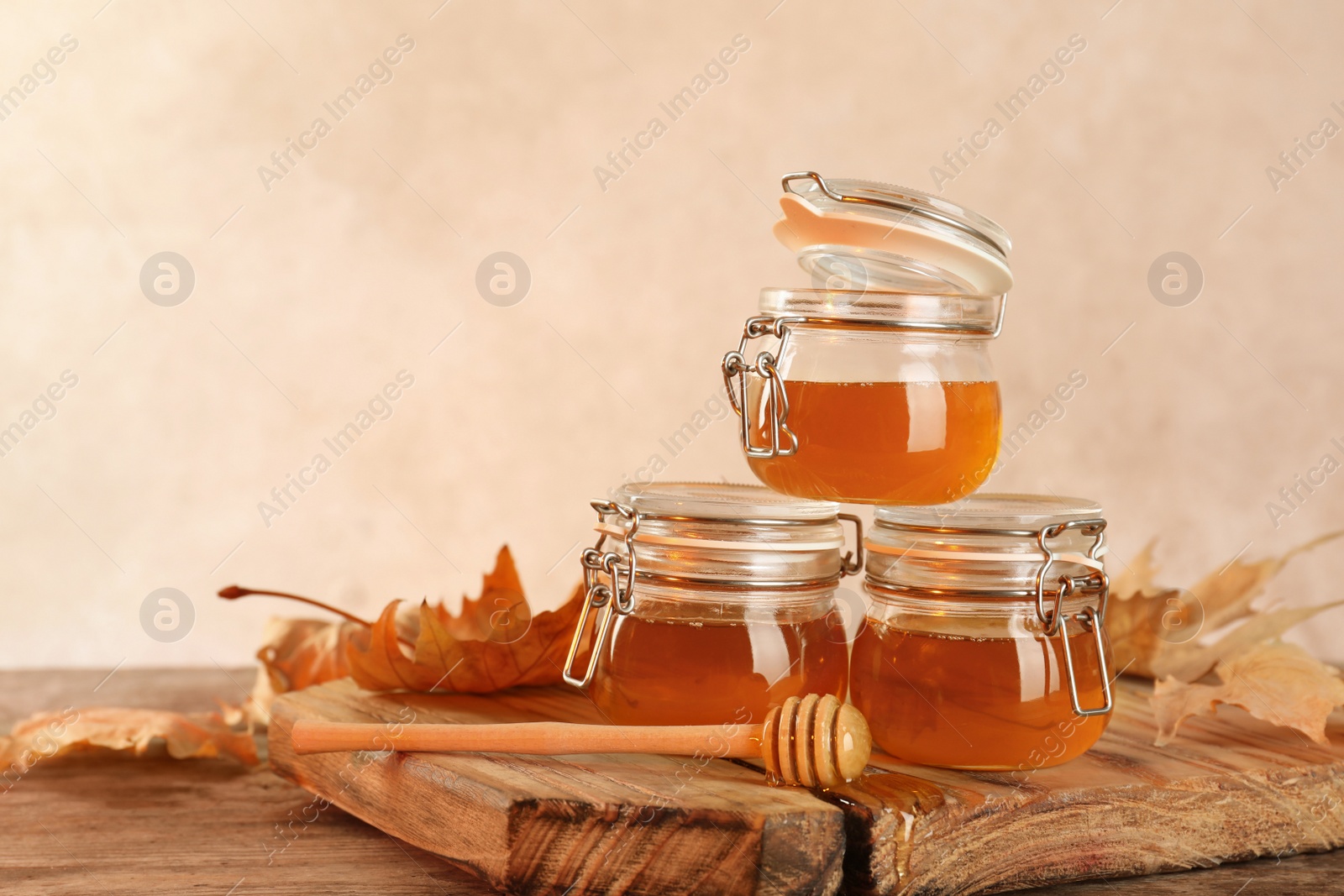 Photo of Dipper and jars with honey on table against color background. Space for text