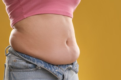 Photo of Woman with excessive belly fat on goldenrod background, closeup. Overweight problem
