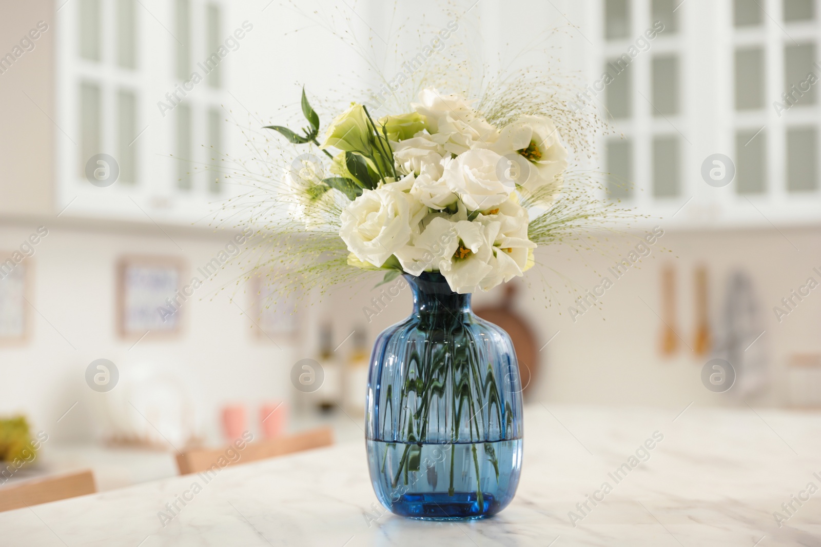 Photo of Bouquet of beautiful eustoma flowers on white table in kitchen. Interior design