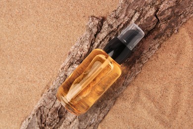 Photo of Bottle of serum and tree bark on sand, top view