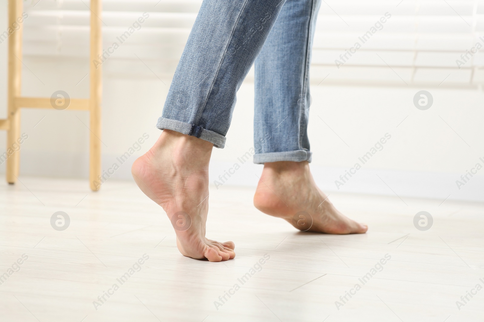 Photo of Barefoot woman walking on white parquet at home, closeup. Heated floor