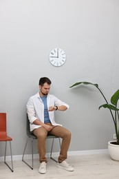 Photo of Man looking at wrist watch and waiting for job interview indoors