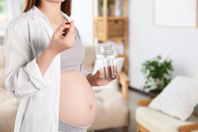 Photo of Pregnant woman holding pill and glass with water at home, closeup