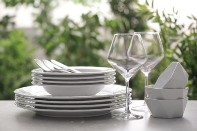 Photo of Set of clean dishware, cutlery and wineglasses on grey table against blurred background