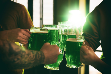 Photo of Group of friends toasting with green beer in pub, closeup. St. Patrick's Day celebration
