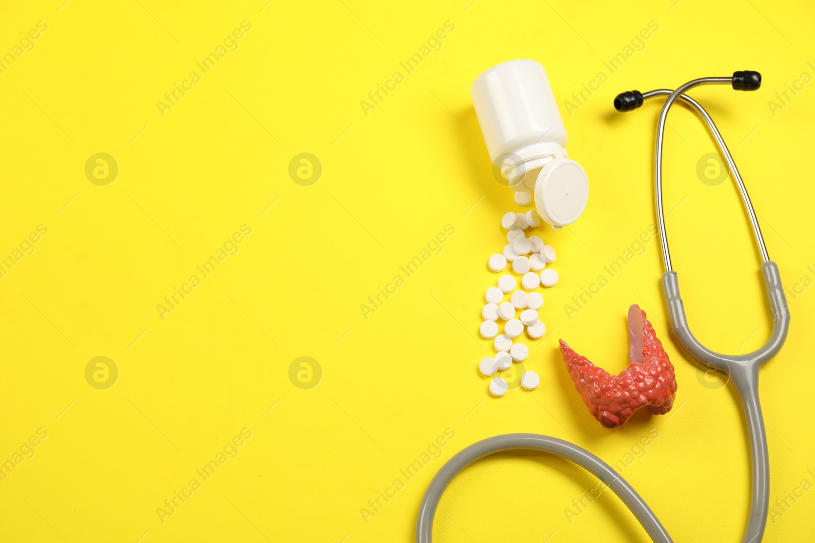 Photo of Endocrinology. Stethoscope, bottle with pills and model of thyroid gland on yellow background, flat lay. Space for text