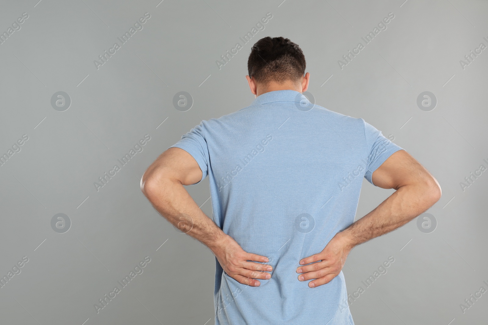 Photo of Man suffering from lower back pain on light grey background. Visiting orthopedist