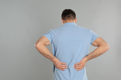 Photo of Man suffering from lower back pain on light grey background. Visiting orthopedist