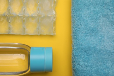 Bottle of water, ice pack and towel on yellow background, flat lay. Heat stroke treatment