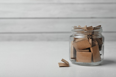 Photo of Glass jar with paper pieces on white table, space for text