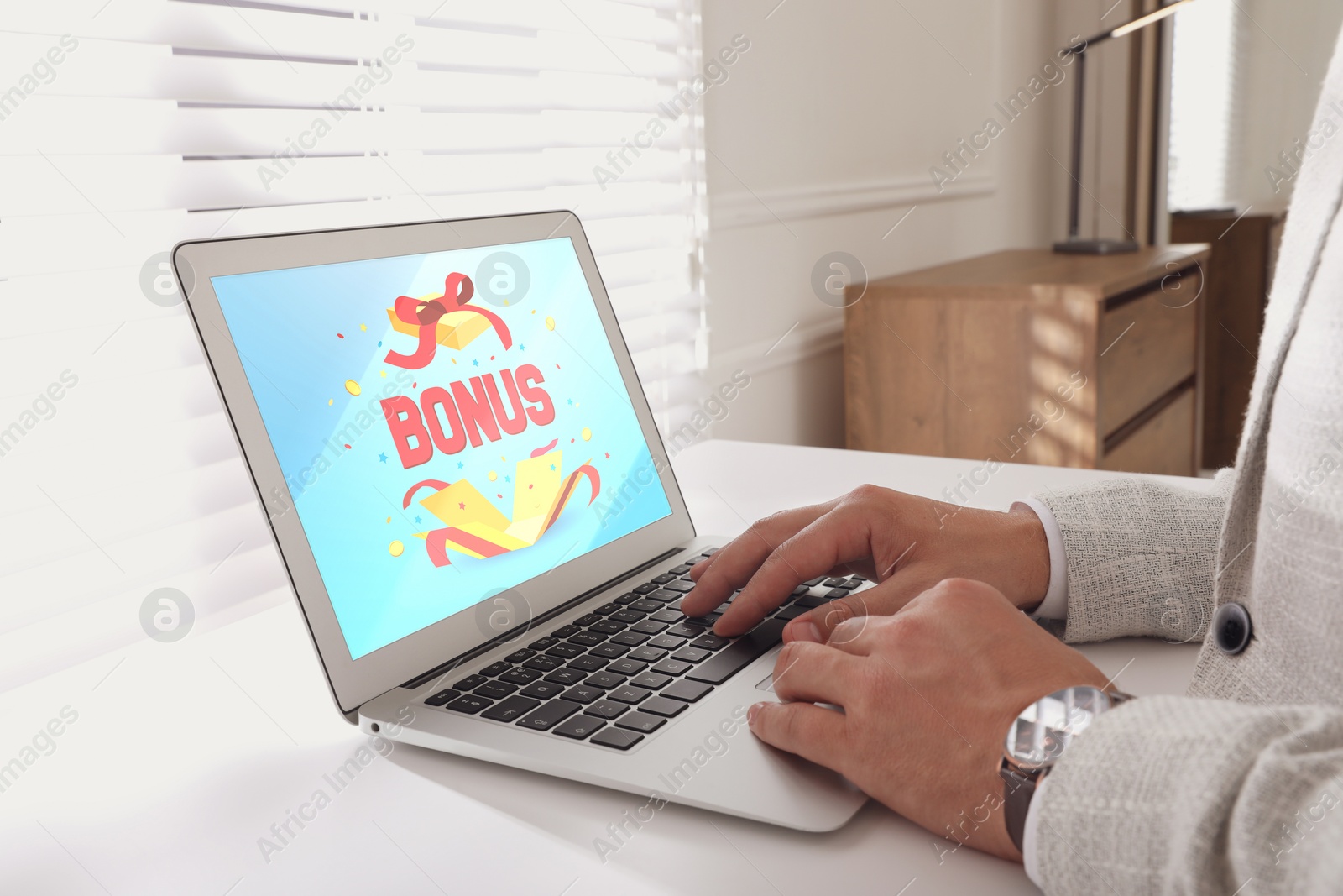 Image of Bonus gaining. Man using laptop at white table indoors, closeup. Illustration of open gift box, word and confetti on device screen