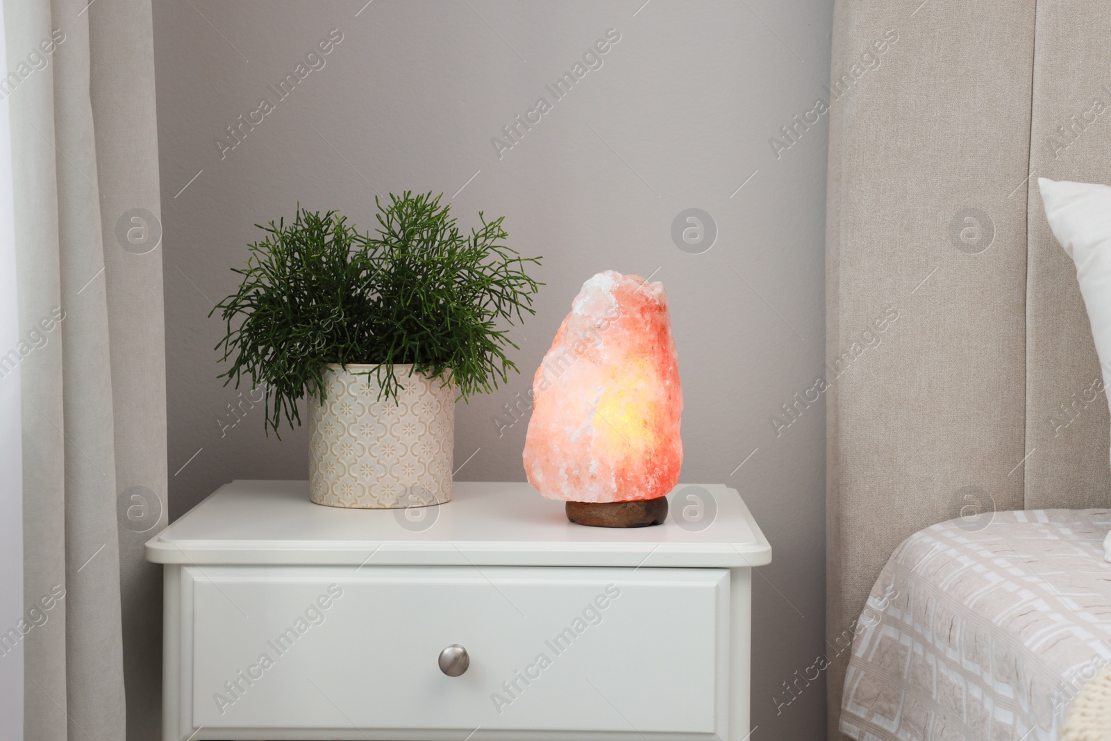 Photo of Beautiful Himalayan salt lamp and green houseplant on white stand in bedroom