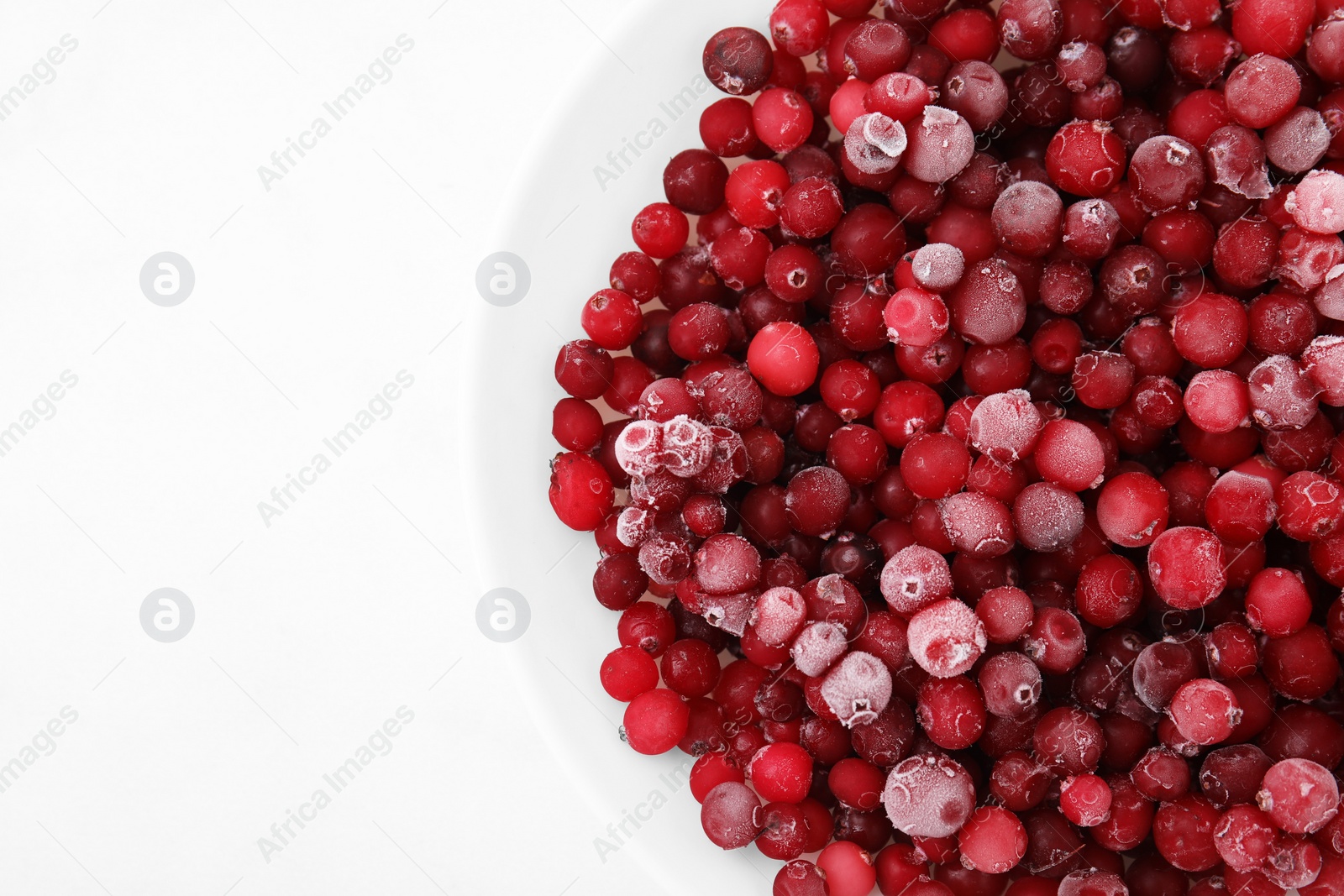 Photo of Frozen red cranberries in bowl on white table, top view. Space for text