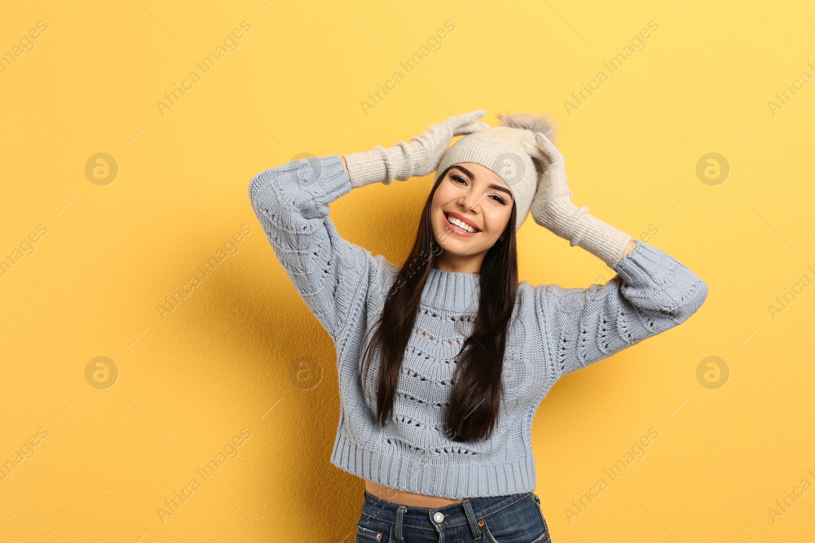 Photo of Happy young woman in warm clothes on yellow background. Winter vacation