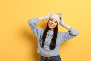 Photo of Happy young woman in warm clothes on yellow background. Winter vacation