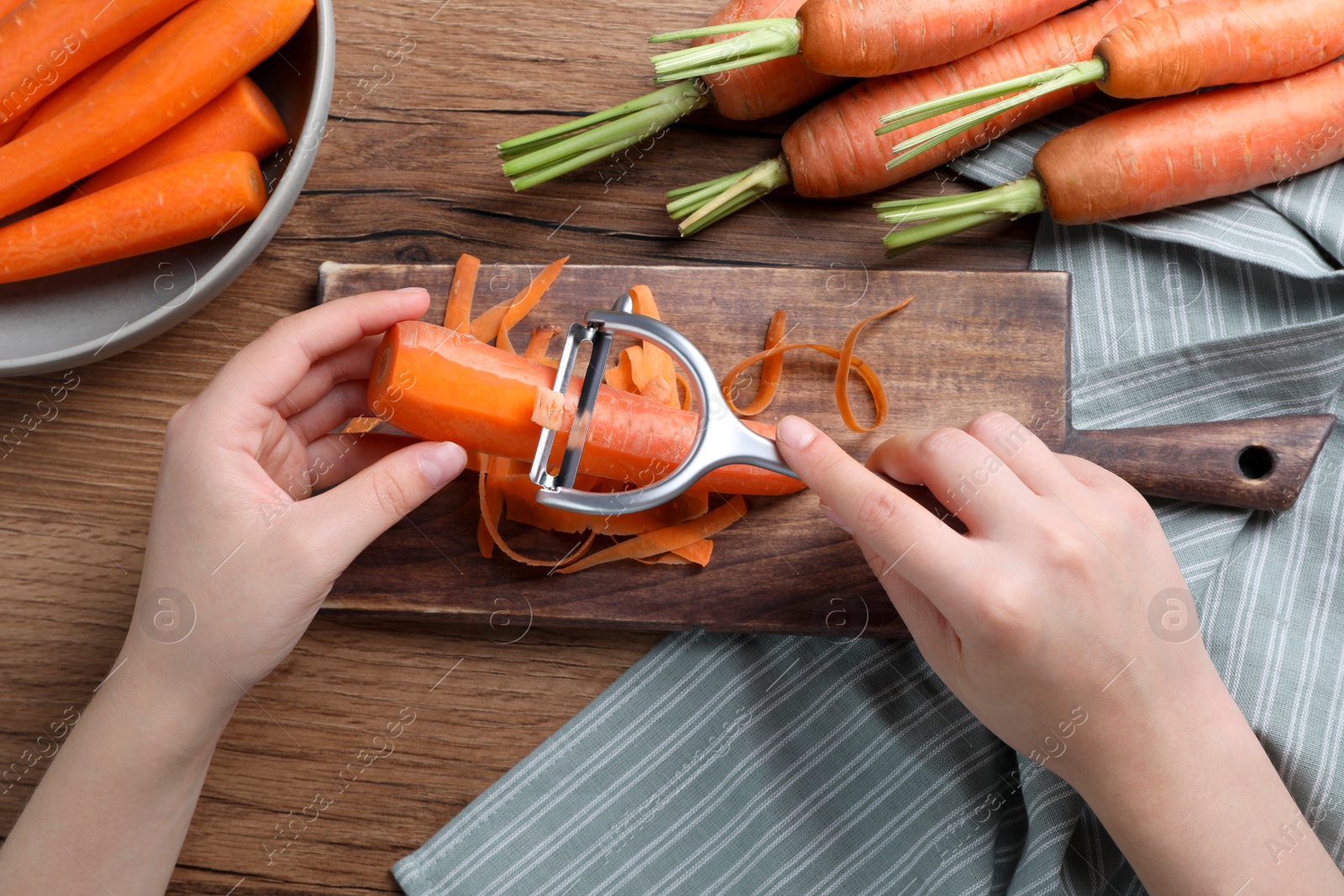 Photo of Woman peeling fresh carrot at wooden table, top view