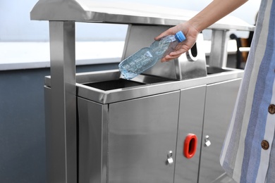 Photo of Woman throwing plastic bottle into recycling bin outdoors, closeup