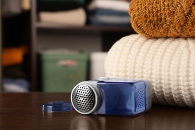 Photo of Fabric shaver near knitted clothes on wooden table indoors, space for text