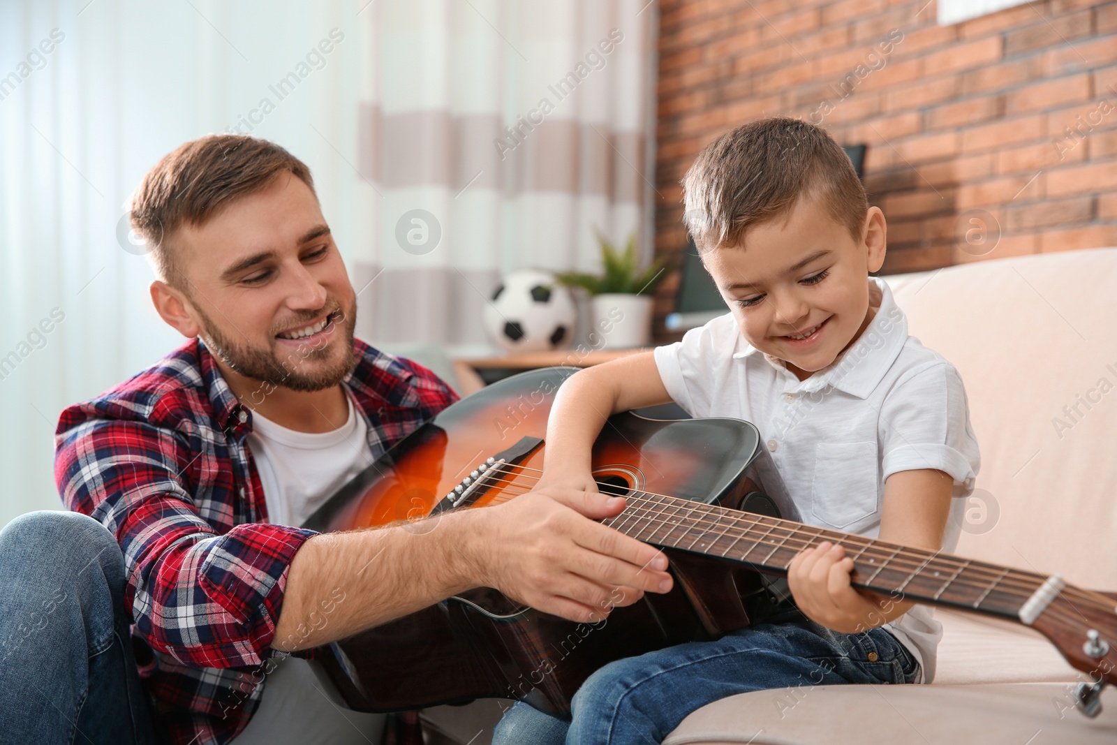 Photo of Father teaching his little son to play guitar at home