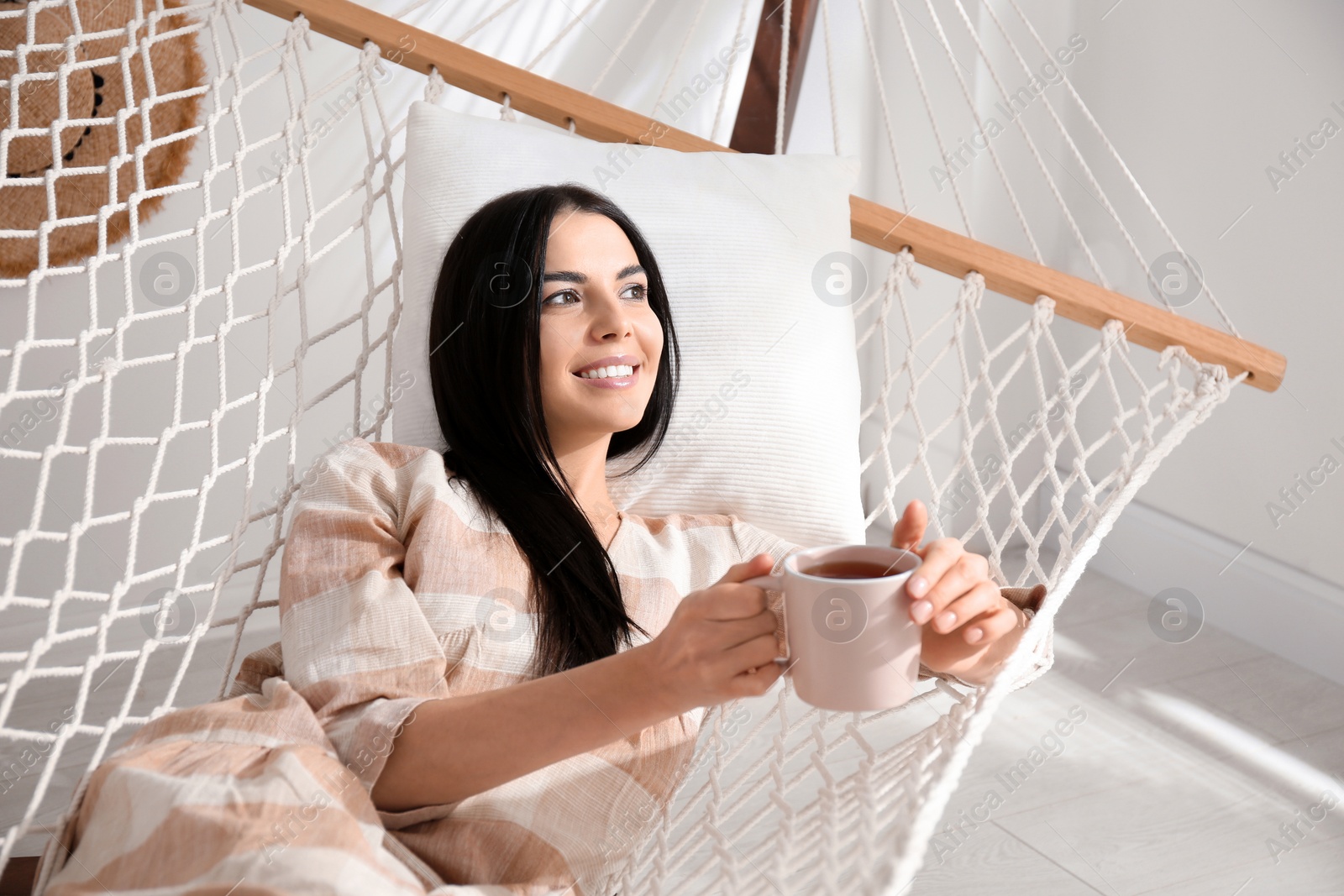 Photo of Young woman with cup of tea in hammock at home