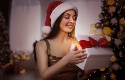 Beautiful woman in Santa hat opening Christmas gift at home