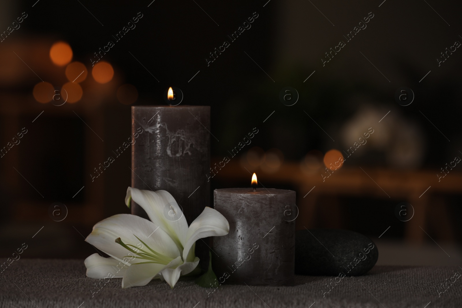 Photo of Spa composition with burning candles, lily flower and stone on massage table in wellness center