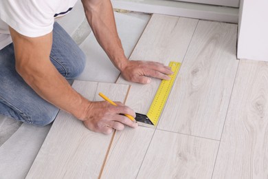 Photo of Man using measuring tape during installation of laminate flooring, closeup