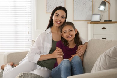 Photo of Young mother and her daughter on sofa in living room. Adoption concept