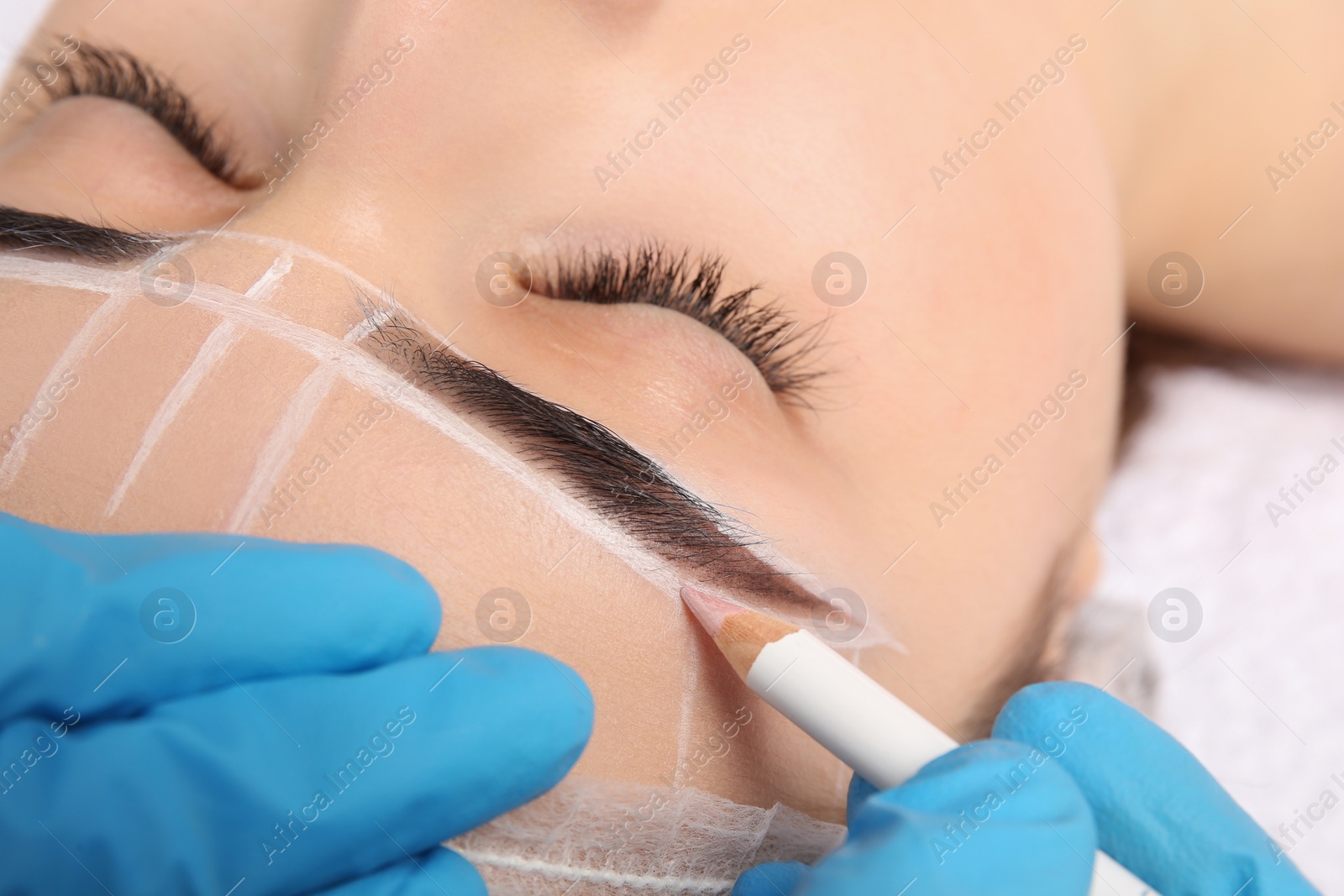 Photo of Cosmetologist preparing young woman for eyebrow permanent makeup procedure, closeup