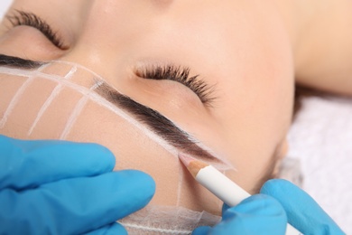 Cosmetologist preparing young woman for eyebrow permanent makeup procedure, closeup