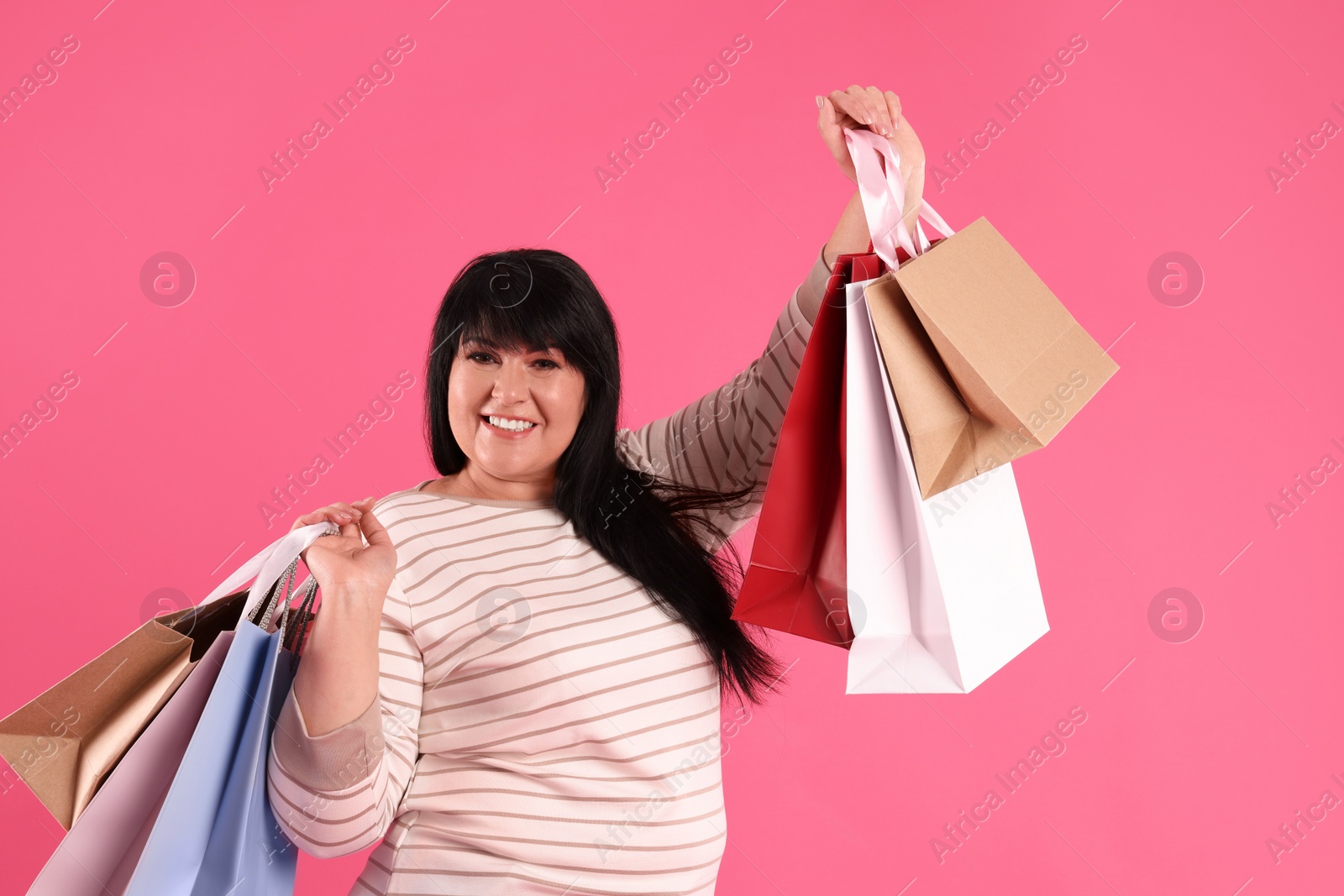 Photo of Beautiful overweight mature woman with shopping bags on pink background