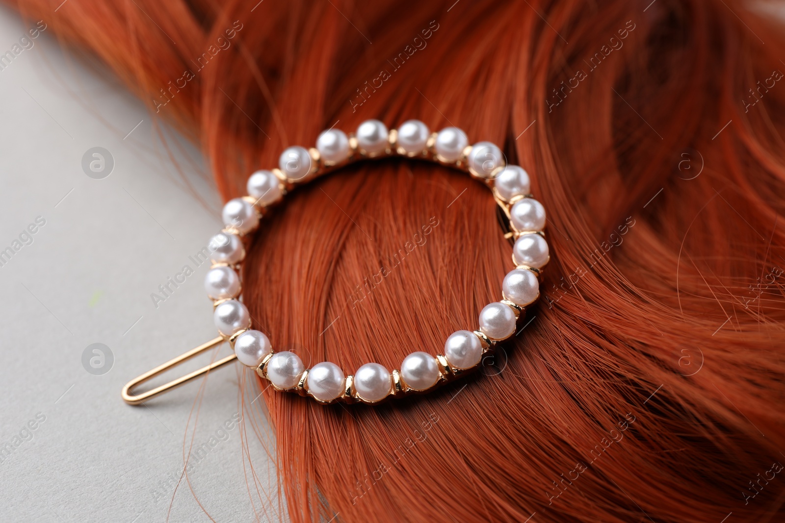 Photo of Elegant pearl clip and red hair strand on white background, closeup