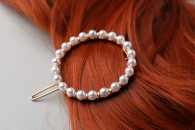 Elegant pearl clip and red hair strand on white background, closeup