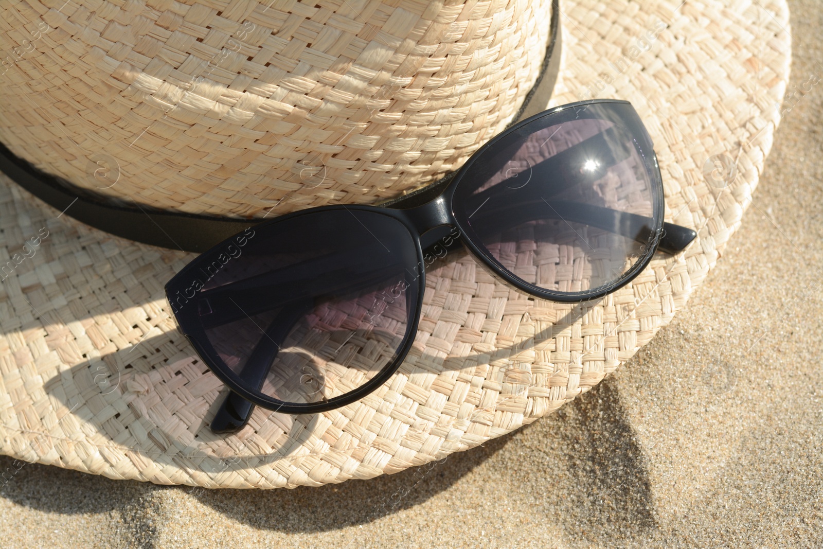 Photo of Hat with beautiful sunglasses on sand, closeup