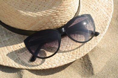 Photo of Hat with beautiful sunglasses on sand, closeup