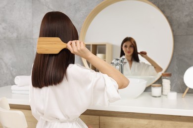 Photo of Beautiful woman brushing her hair near mirror in bathroom