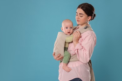 Mother holding her child in sling (baby carrier) on light blue background. Space for text