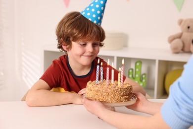 Birthday celebration. Mother holding tasty cake with burning candles near her son indoors